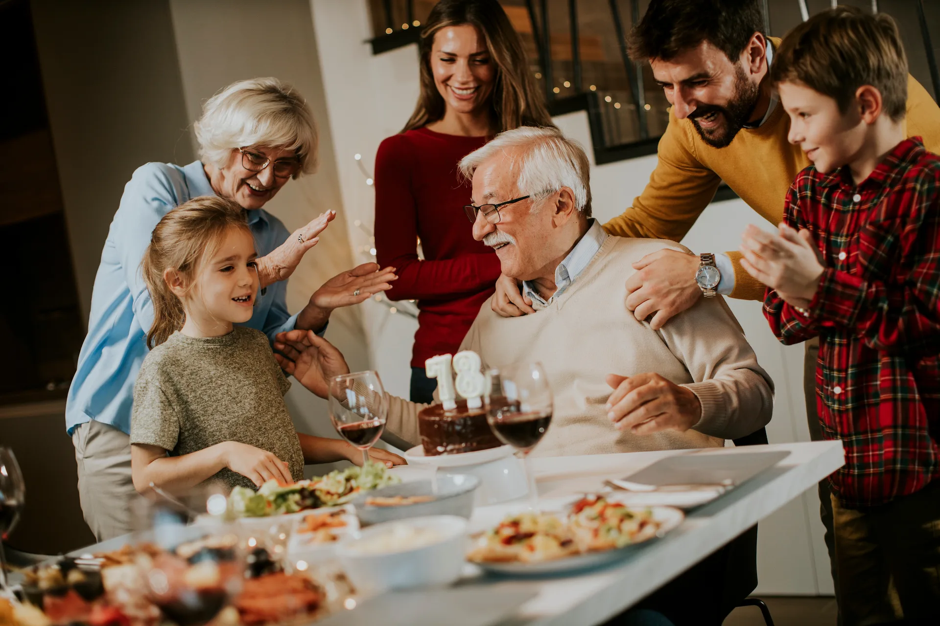 A multi-generational family enjoys a meal together, laughing and interacting joyfully around a dining table. This gathering highlights the industry of home-cooked meals that brings families together.