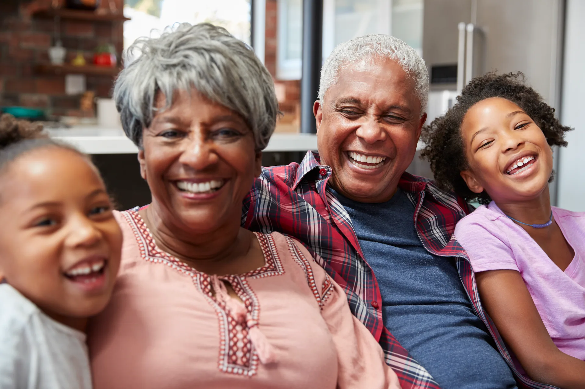 A joyful elderly couple laughing with two young children in a cozy home setting, exemplifying the warmth of dementia care.